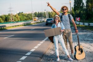 Para młodych podróżników przy drodze zatrzymująca samochód - autostop