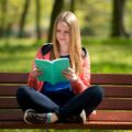 Nastolatka czytająca książkę na ławce w parku